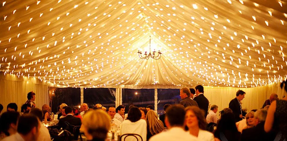 Fairy lights strung across the lined ceiling of a marquee at night