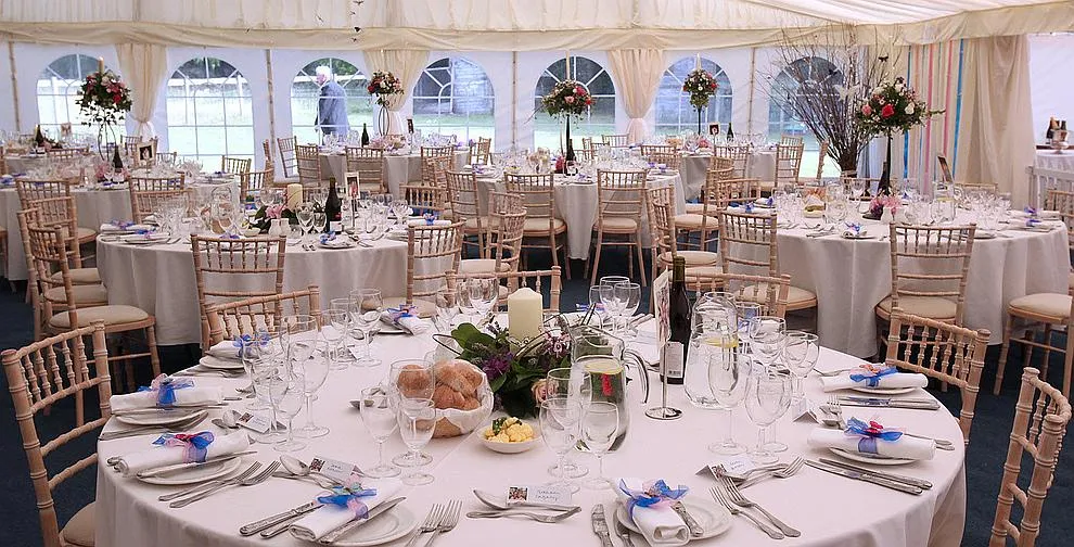 A framed marquee laid up with round tables, linen and chairs ready for guests